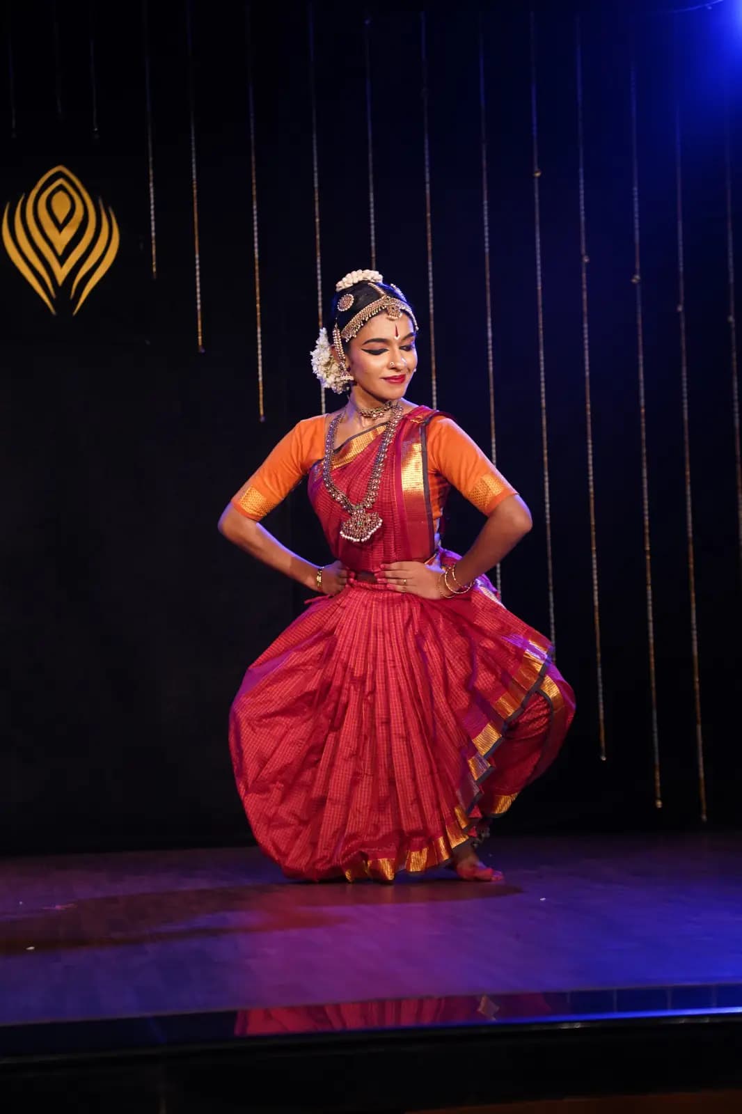 Devi Nandana performing a seated classical dance posture on stage.